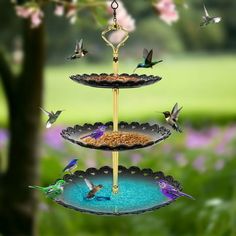 three tiered bird feeder with hummings flying around it and flowers in the background