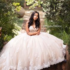 a woman in a wedding dress is sitting on a stone wall and posing for the camera