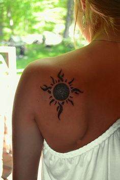 the back of a woman's shoulder with a sun tattoo on it