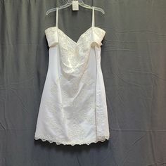 a white dress hanging on a hanger in front of a gray wall with a black background