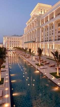 the hotel is lit up at night with lights reflecting in the pool and palm trees