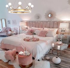 a bedroom decorated in pink and white with lots of decorations on the bed, chandelier