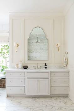 a white bathroom with marble counter tops and two mirrors on the wall, along with gold fixtures