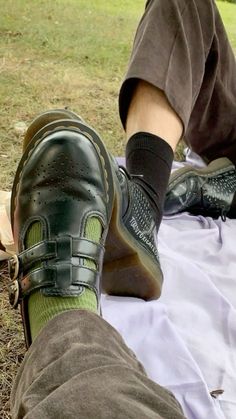 a person wearing green socks and black shoes sitting on a blanket in the grass with their feet up