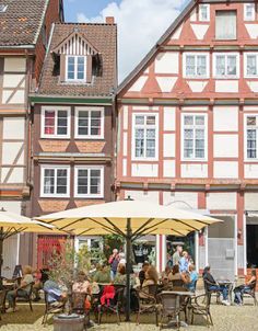 people are sitting at tables outside in front of some old buildings with umbrellas over them