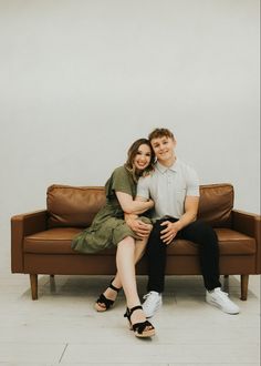 a man and woman sitting on top of a couch next to each other in front of a white wall