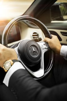 a man in a suit driving a car with his hands on the steering wheel,