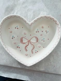 a heart shaped dish with pink bows and hearts on the inside is sitting on a piece of paper