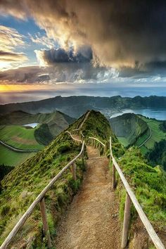 a path leading up to the top of a hill with green hills in the background