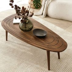 a wooden table sitting on top of a white rug next to a vase filled with flowers