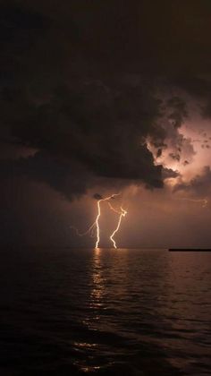 lightning striking over the ocean with dark clouds and bright lights in the sky above it