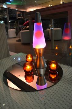 a table topped with three lit candles on top of a glass plate next to a mirror