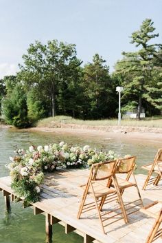 chairs are set up on the dock for an outdoor wedding ceremony with flowers and greenery