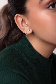 a woman wearing a pair of ear cuffs and a green turtle - neck sweater is looking off into the distance