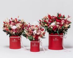 three red buckets filled with flowers on top of a white table next to each other