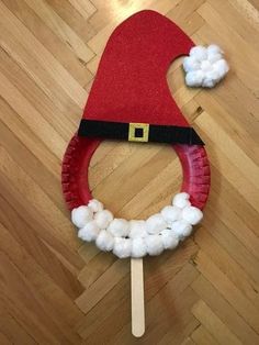 a paper plate santa hat with cotton balls around it on a wooden floor next to a toothpick