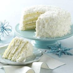 a white cake with coconut frosting on a plate next to a slice cut from it