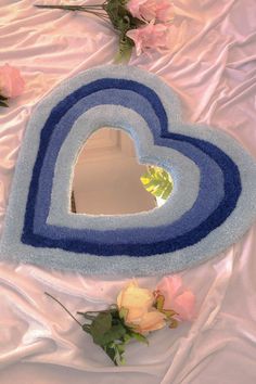 a blue heart shaped mirror sitting on top of a white sheet next to pink flowers