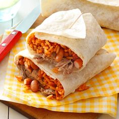 two burritos with meat and beans are sitting on a yellow checkered napkin