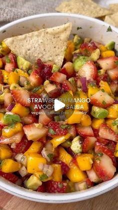 a white bowl filled with fruit salsa and tortilla chips on top of a wooden cutting board