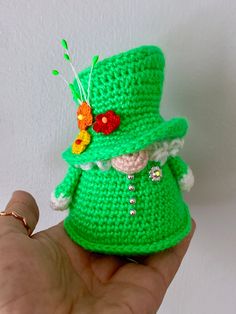 a small crocheted green hat with flowers on it's head is being held by a hand