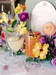 two cocktails are sitting on a table with flowers in front of the drinks glasses