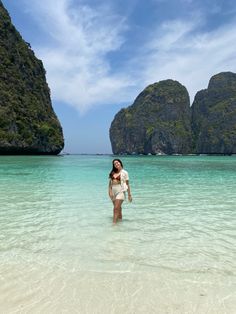 a woman standing in shallow water near the shore with mountains and rocks in the background