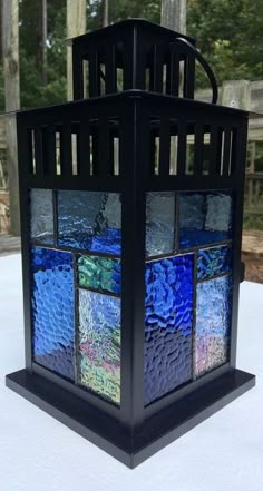 a stained glass lantern sitting on top of a white tablecloth covered table with trees in the background