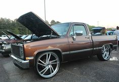 a brown truck with its hood open parked in a parking lot next to other cars