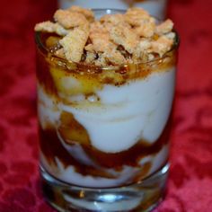 two glasses filled with dessert sitting on top of a red tablecloth covered table cloth