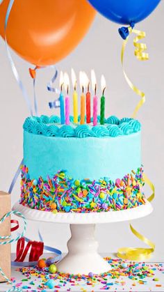 a birthday cake with blue frosting and colorful sprinkles, balloons and streamers