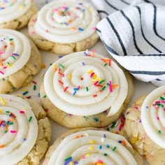 cookies with white frosting and sprinkles on a table next to a towel