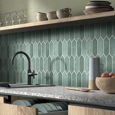 a kitchen counter with dishes and cups on the shelf above it, in front of a green tiled backsplash