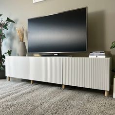 a flat screen tv sitting on top of a white cabinet in front of a plant