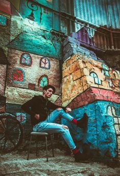 a man sitting on top of a chair next to a wall covered in colorful graffiti