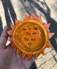 a hand holding an orange sun shaped vase with writing on it