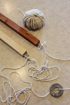 two balls of yarn are on the floor next to a ball of string and a piece of wood