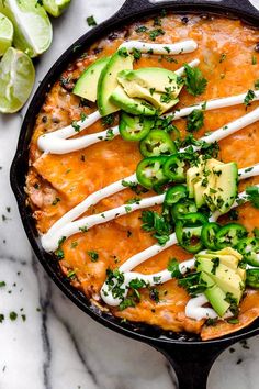 an enchilada in a cast iron skillet topped with avocado and sour cream