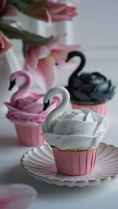 two cupcakes with frosting and swans on them sitting on a saucer