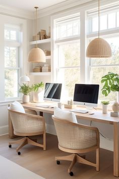 a desk with two computers on it in front of three large windows and some plants