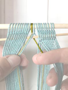 two hands are holding yarn on a wooden skewer and one hand is knitting the thread