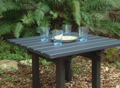 a table with three glasses on it in the middle of some plants and dirt ground