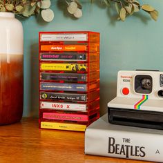 a polaroid camera sitting on top of a stack of books next to a vase with flowers