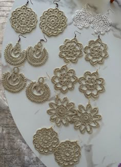 several pairs of earrings on a white plate next to flowers and lace doilys