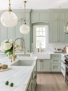 a kitchen with green cabinets and white counter tops, two hanging lights above the sink