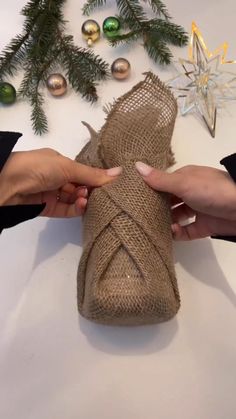 two hands holding a wrapped present in burlock and twine with christmas decorations around it