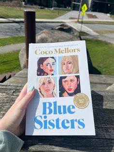 a person holding up a copy of the book blue sisters by coco mellors