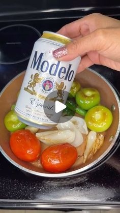 a can of modelo sits in a pan filled with tomatoes, peppers and onions