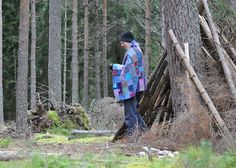 a man standing next to a pile of logs in the woods with a blanket over his head