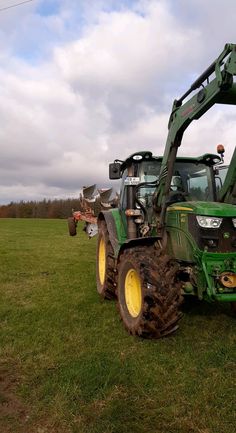 two green tractors parked in a field on a cloudy day